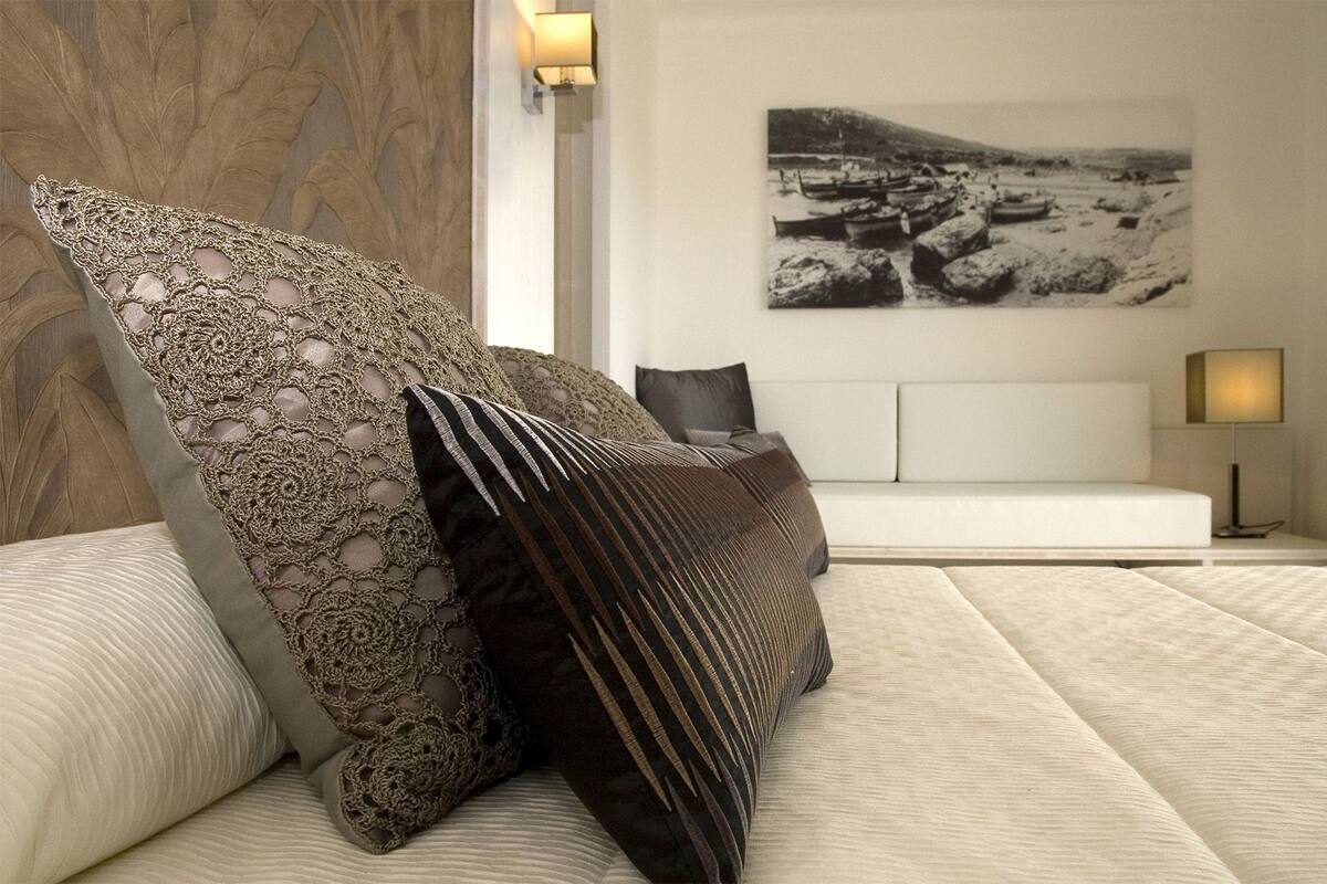 A modern bedroom with a large bed, decorative pillows, a wall-mounted lamp, and a framed photograph.