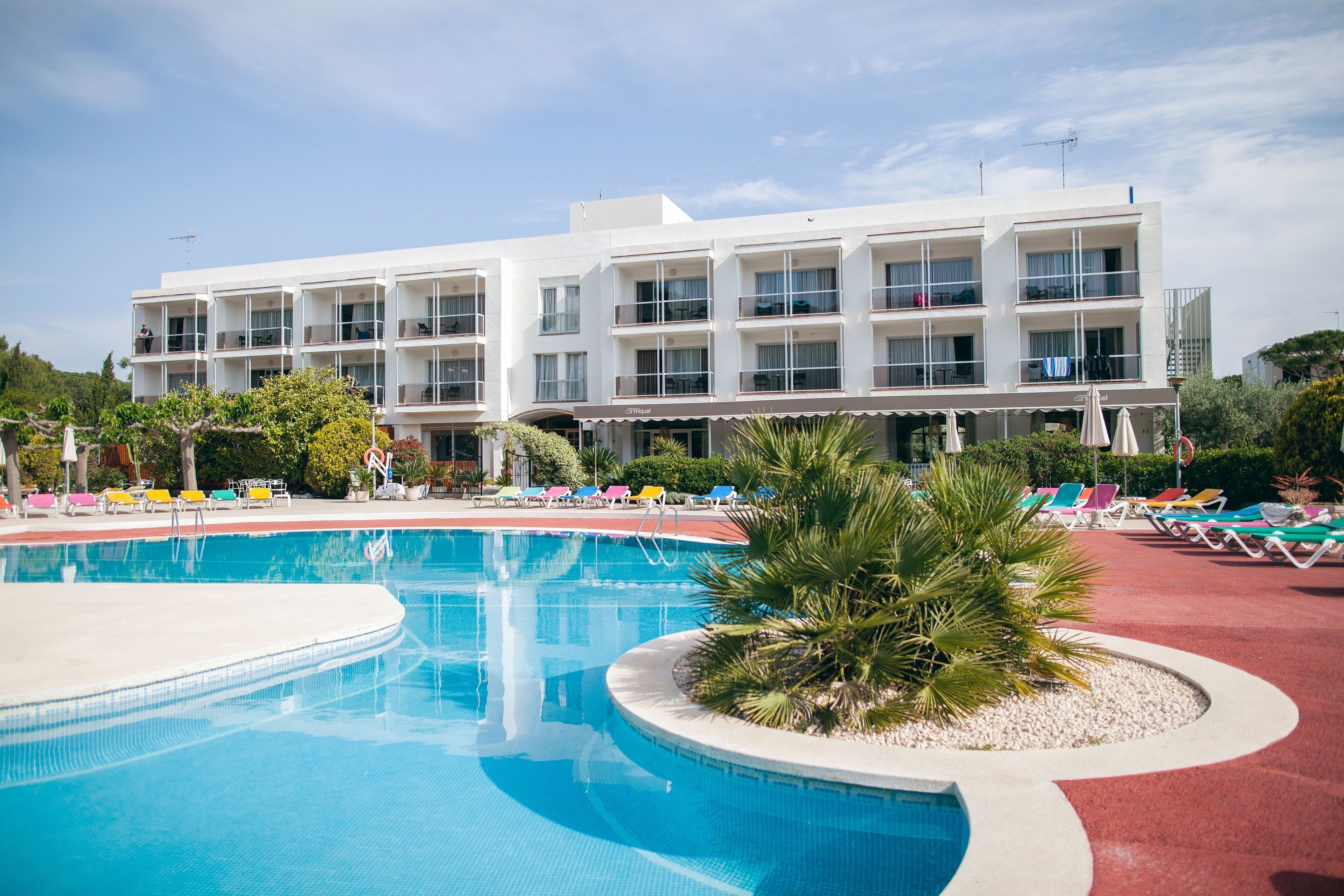 Un hotel con piscina, varios balcones y sillas de descanso coloridas.