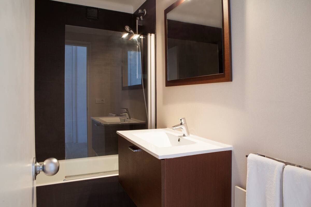 A modern bathroom with a white sink, dark wooden vanity, and a large mirror.