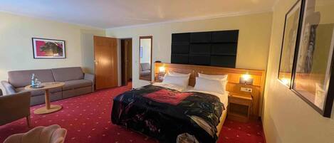 Una habitación de hotel con cama, sofá, sillón, una mesita y una mesita de noche.