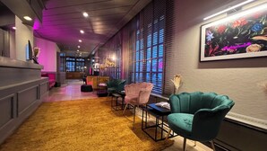 A modern lounge area with a yellow shag rug, teal armchairs, and a large window with blinds. - Das Seela Braunschweig (Braunschweig)