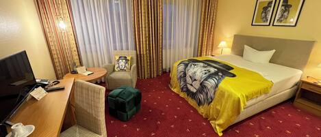 Una habitación de hotel con una cama, un escritorio con una computadora, una silla, una mesita y una lámpara.