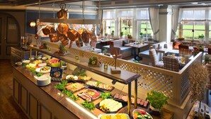 A buffet with a variety of food options, a seating area with tables and chairs, and large windows with a view of the outdoors. - Das Seela Braunschweig (Braunschweig)