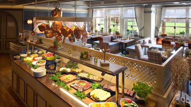 A buffet with a variety of food options, a seating area with tables and chairs, and large windows with a view of the outdoors. - Das Seela Braunschweig (Braunschweig)