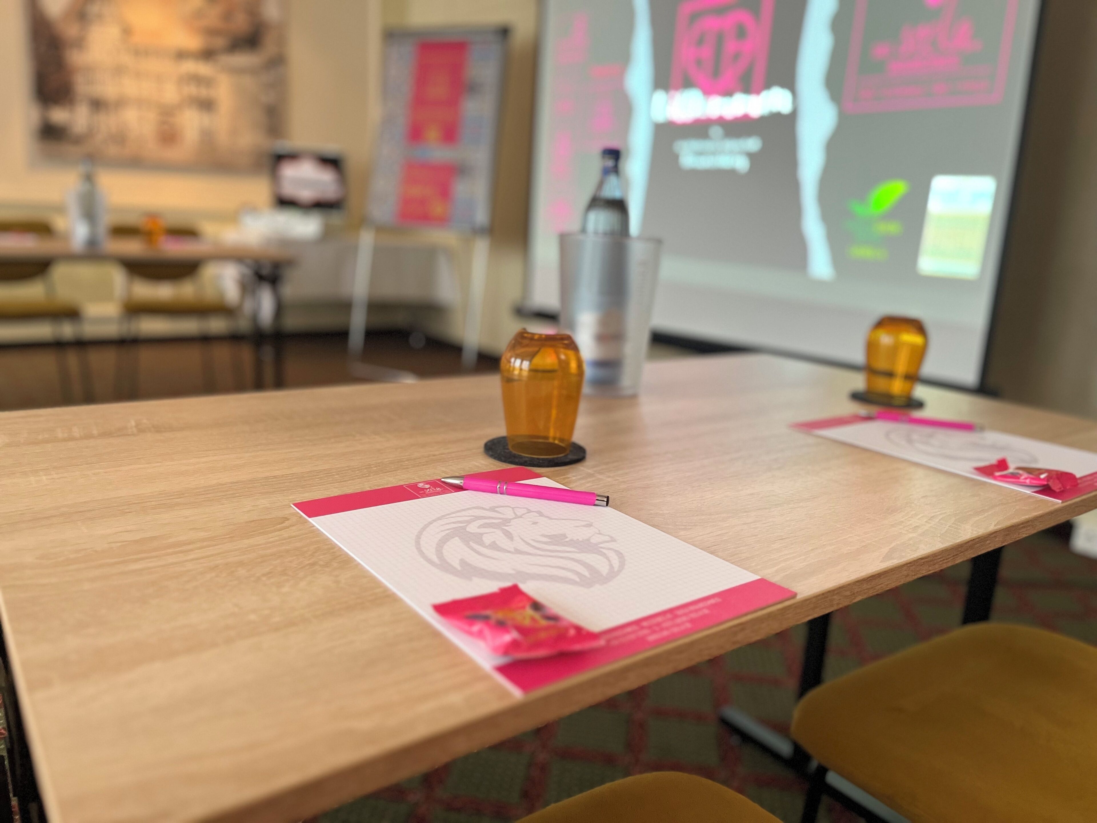 A conference room with a long table, two chairs, a projector screen, and a bottle on the table.
