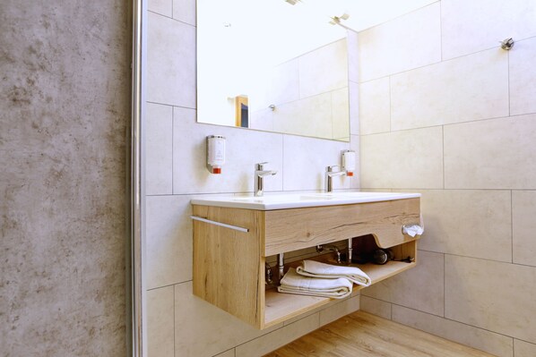 A modern bathroom with a wooden vanity, a large mirror, and a towel rack. - Das Seela Braunschweig (Braunschweig)
