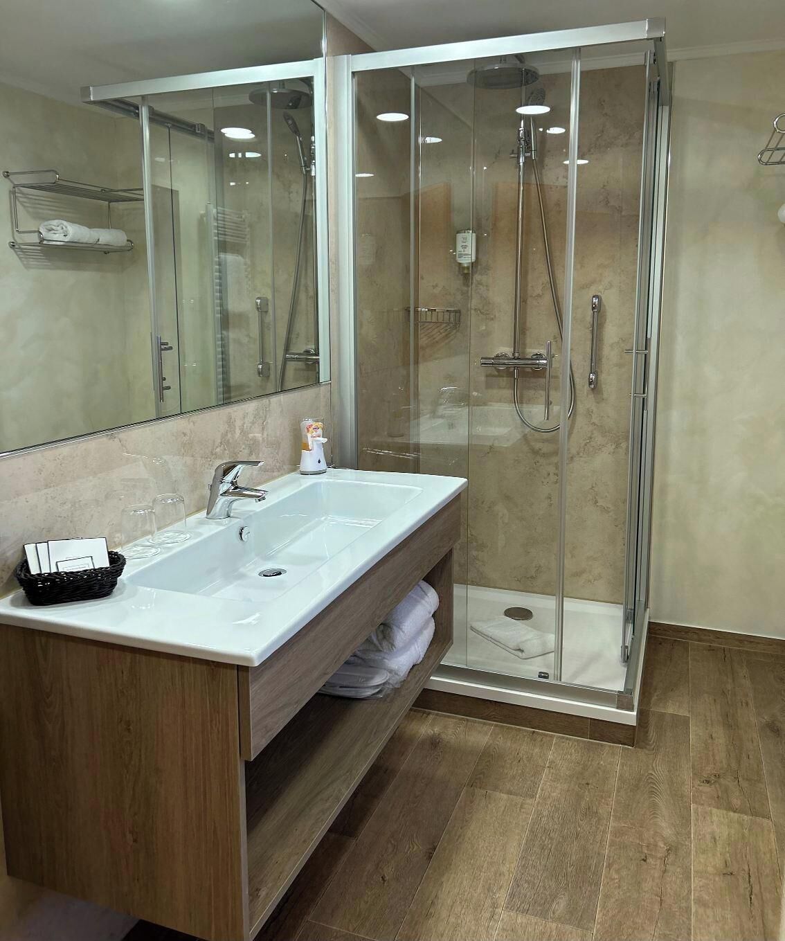 A modern bathroom with a glass-enclosed shower, a wooden vanity with a large sink, and a mirror.