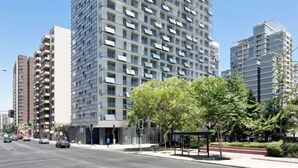 A modern high-rise building with a glass facade, multiple balconies, and a clear sky. - Gen Rooms (Santiago)