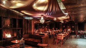 A restaurant with wooden walls, leather seating, and chandeliers. - Gen Rooms (Santiago)