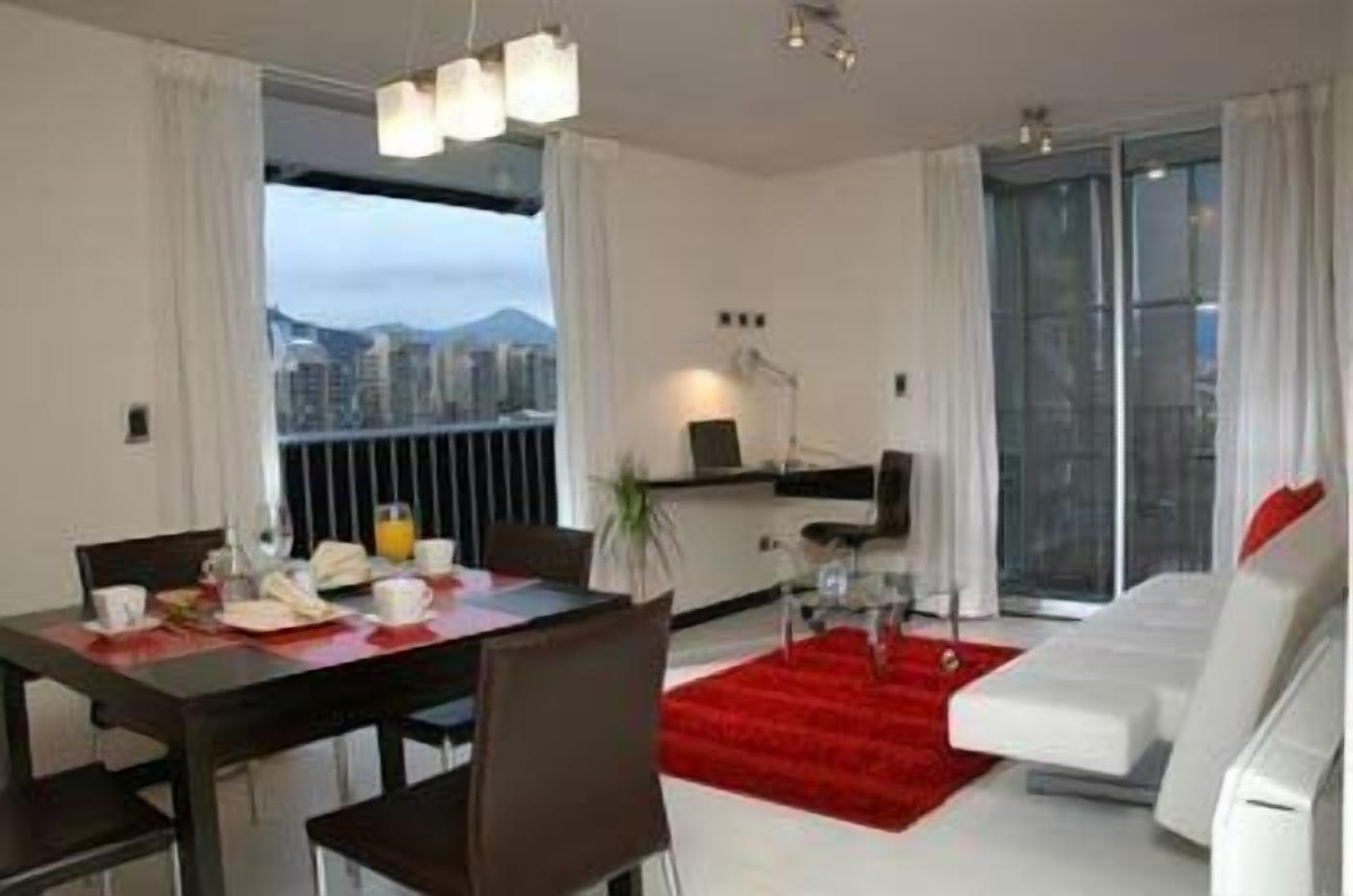 A modern living room with a dining area, large windows, and a city view.