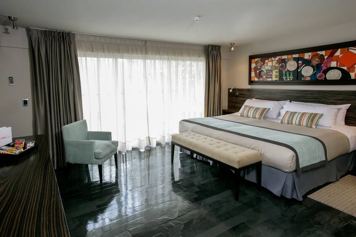 A modern hotel room with a large bed, a bedside table, a chair, and a large window with curtains.