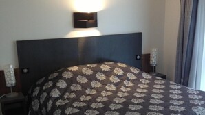Habitación de hotel con una cama grande, una mesita de noche, una lámpara de pared y una ventana con cortinas.