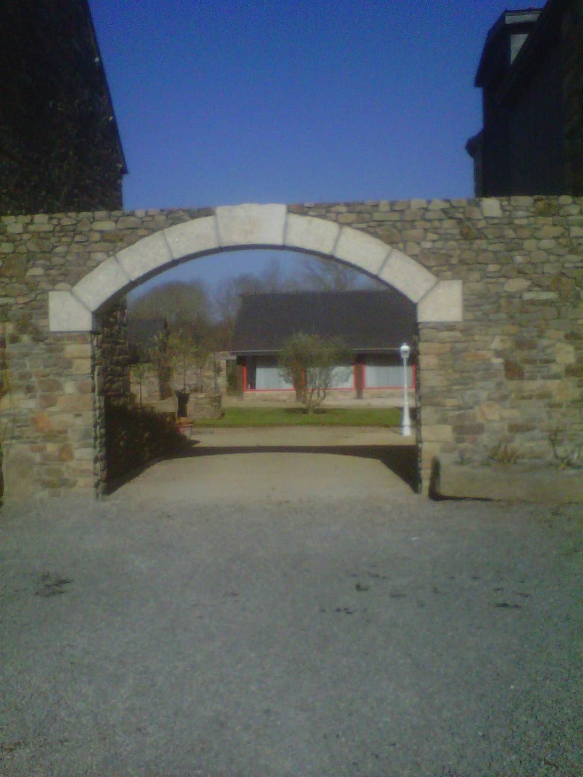 A stone archway leading to a building with a red door.