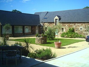 A residential property with a stone building, a patio with outdoor furniture, and a well-maintained lawn. - Manoir De Kermodest (Quemper-Guezennec)