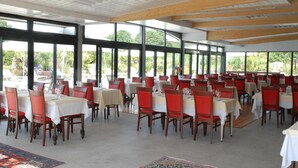 Un amplio comedor interior con varias mesas y sillas, y ventanas grandes que ofrecen vistas a la vegetación.