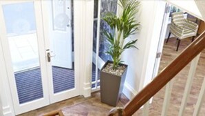 A staircase leading to a landing with a potted plant, a door with glass panels, and a view of the outdoors.