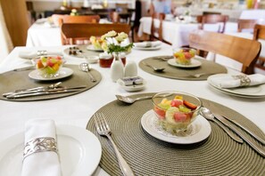 A dining area with tables set for a meal, including plates, cutlery, and a fruit dessert. - Yamkela Guest House (Oudtshoorn)