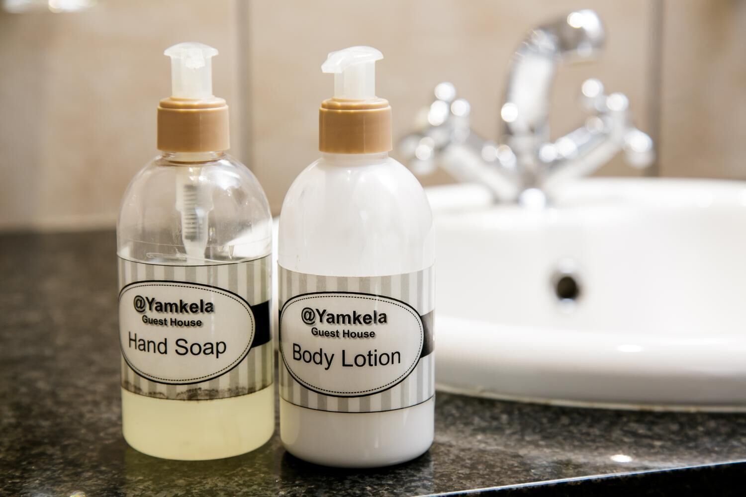 Two bottles of hand soap and body lotion on a countertop with a sink in the background.