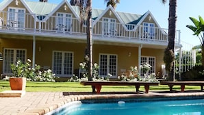 A pool area with a clear blue pool, a patio with a bench, and a building with a balcony and windows.