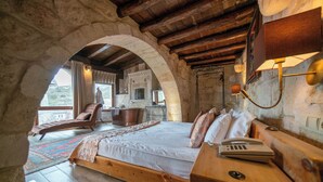 Un dormitorio con una cama grande, una mesita de noche de madera, un teléfono y un arco de piedra.