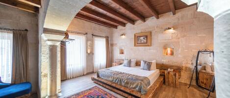 A bedroom with a large bed, a wooden bench, a patterned rug, stone walls, and a stone fireplace.