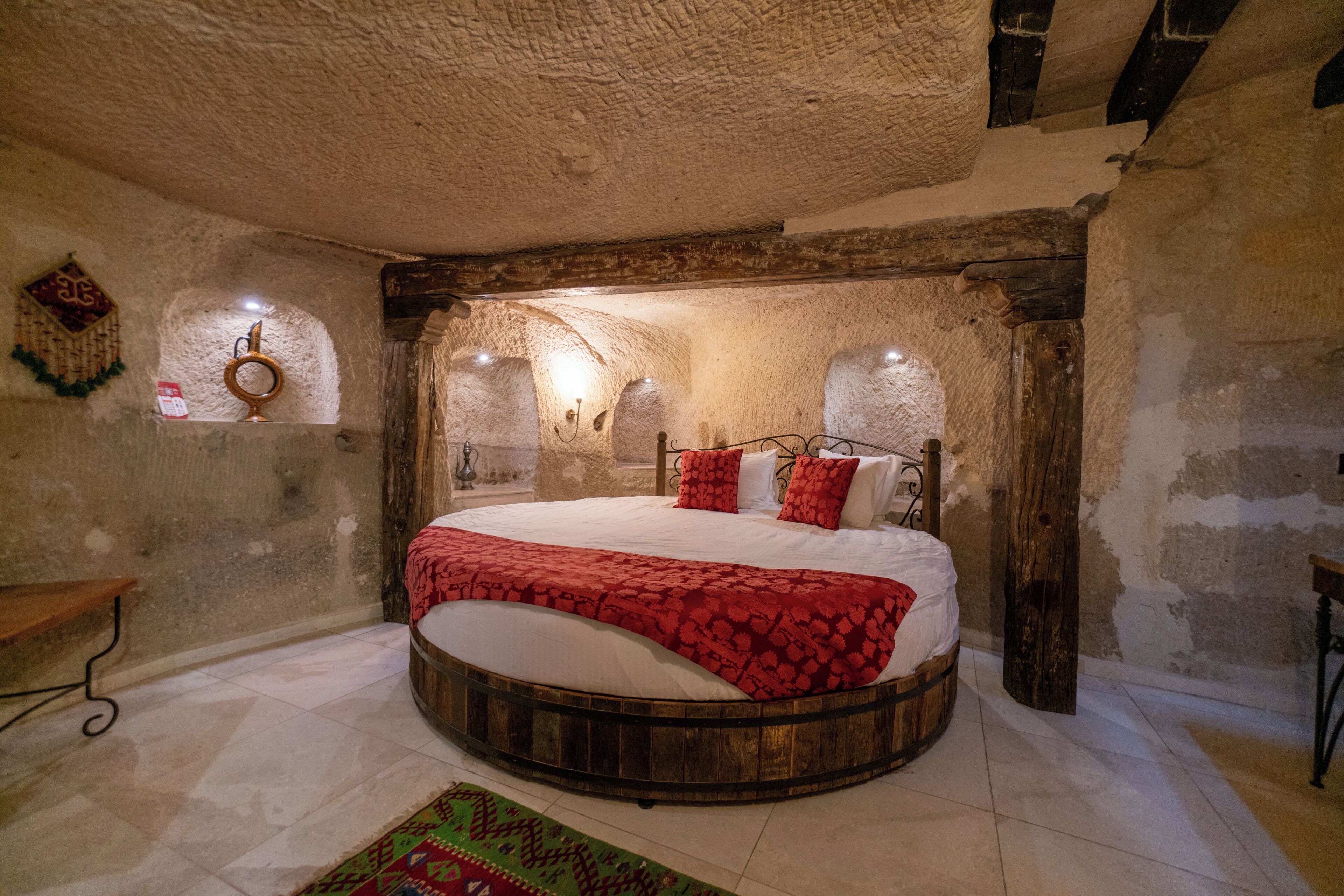 Una cama redonda de madera en una habitación rústica con paredes de piedra y un ventanal pequeño.