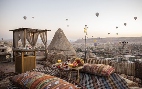 A rooftop terrace with a dining table set for breakfast, a decorative lamp, and a view of the city with hot air balloons in the distance.