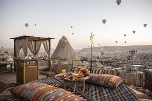 A rooftop terrace with a dining table set for breakfast, a decorative lamp, and a view of the city with hot air balloons in the distance. - Divan Cave House (Nevsehir)