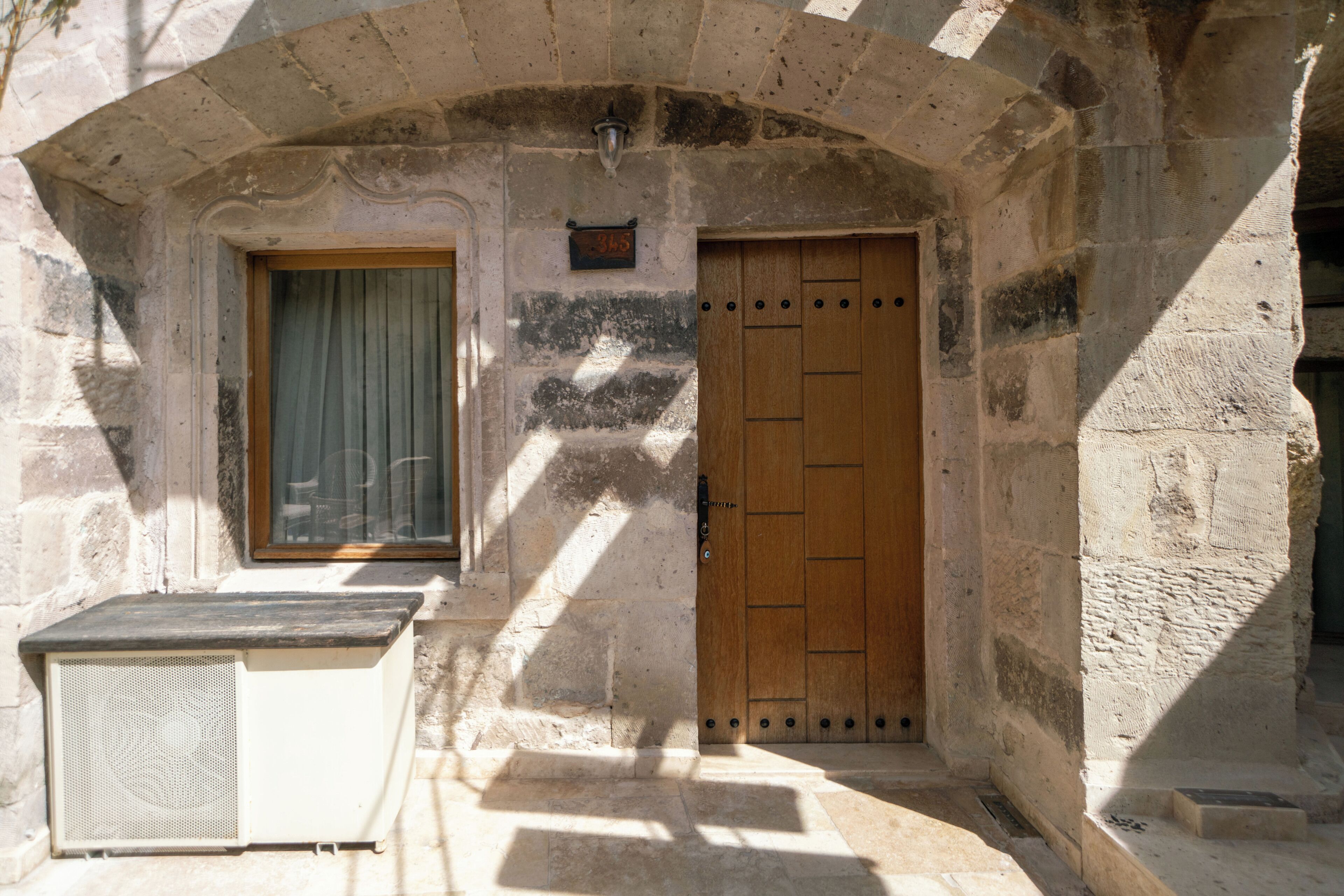 An arched doorway with a wooden door, a window with a curtain, and a small air conditioning unit.
