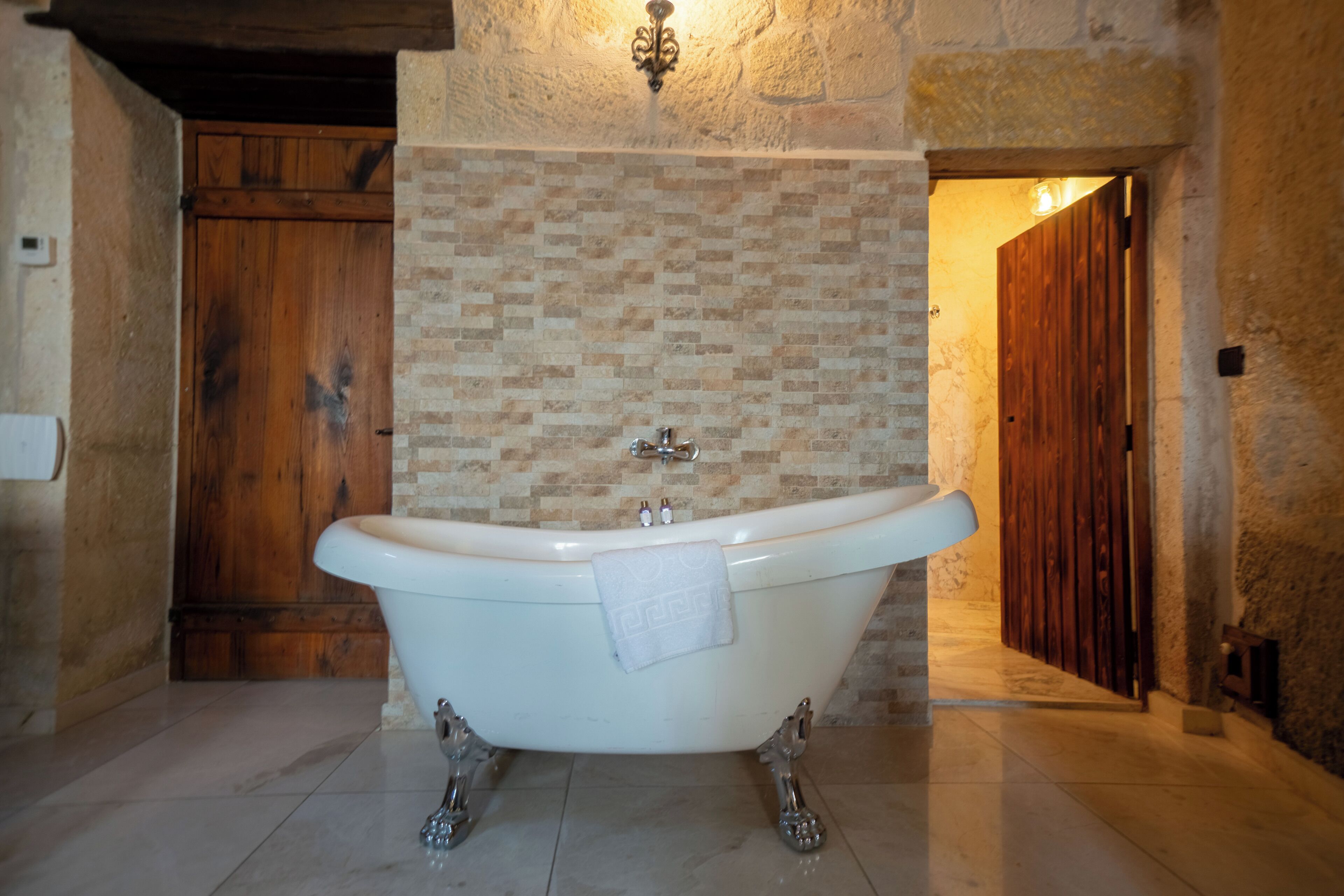 A bathroom with a freestanding bathtub, a wooden door, and a stone wall.