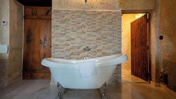 Un baño con una bañera independiente, una puerta de madera y una pared de piedra.