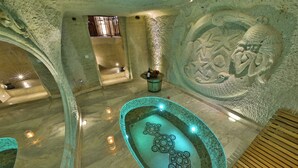 Un área de spa con un jacuzzi de mosaicos, paredes de piedra y velas.