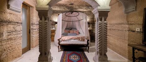 Una habitación con una cama con dosel, una alfombra estampada y paredes de piedra.