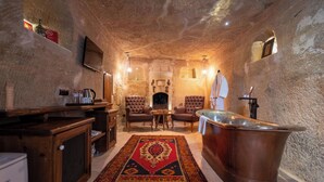 Una habitación con paredes de piedra, una bañera, dos sillones, una mesa de centro y una chimenea.