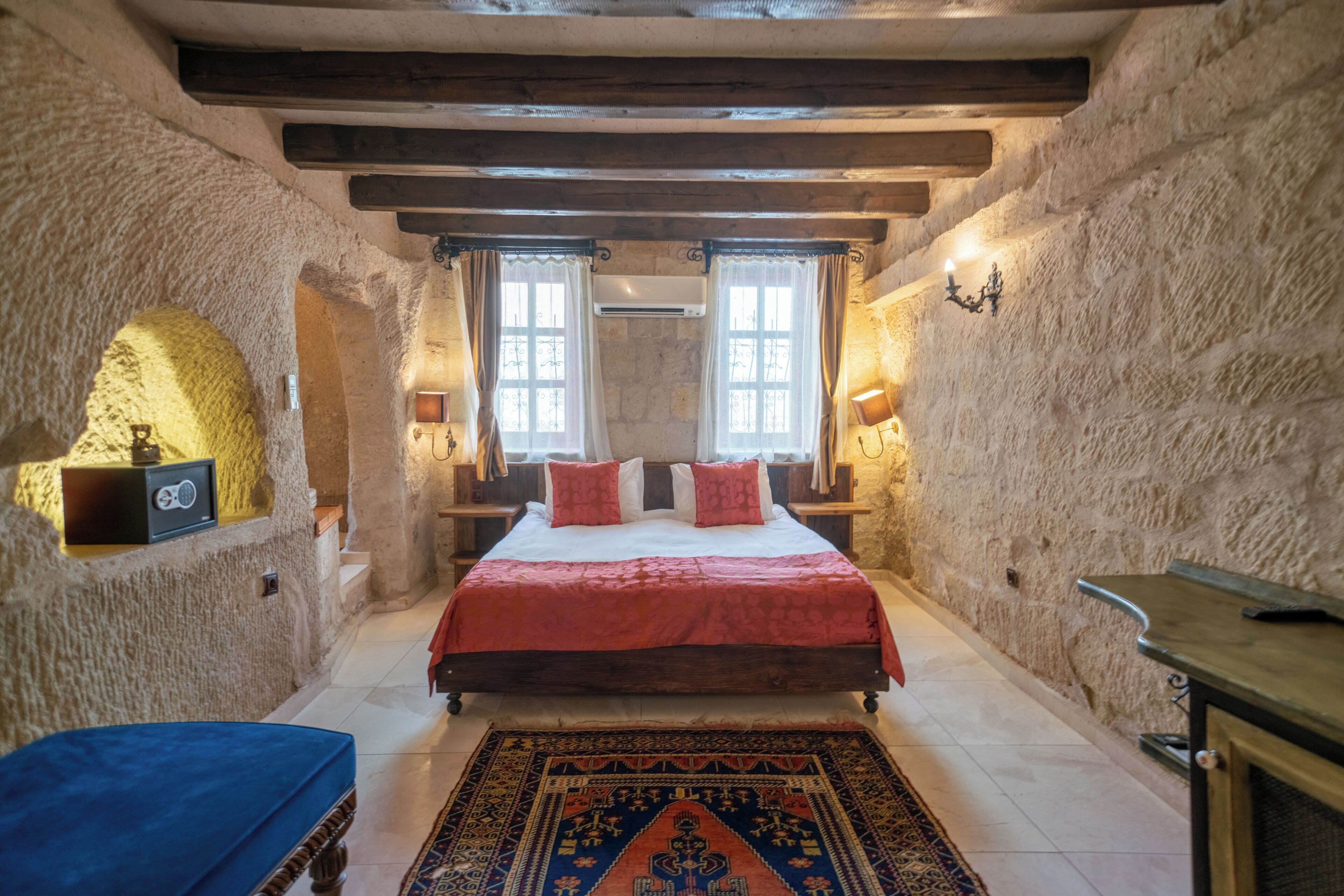 A bedroom with a bed, two windows, a rug, and stone walls.