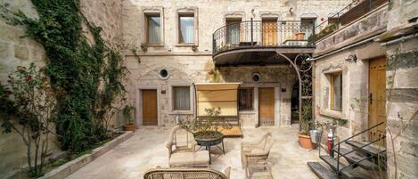 Un patio con muros de piedra, una escalera de madera, muebles de mimbre y plantas en macetas.