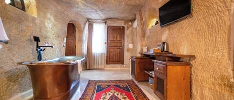 A bathroom with a bathtub, wooden cabinets, a television, and a patterned rug.