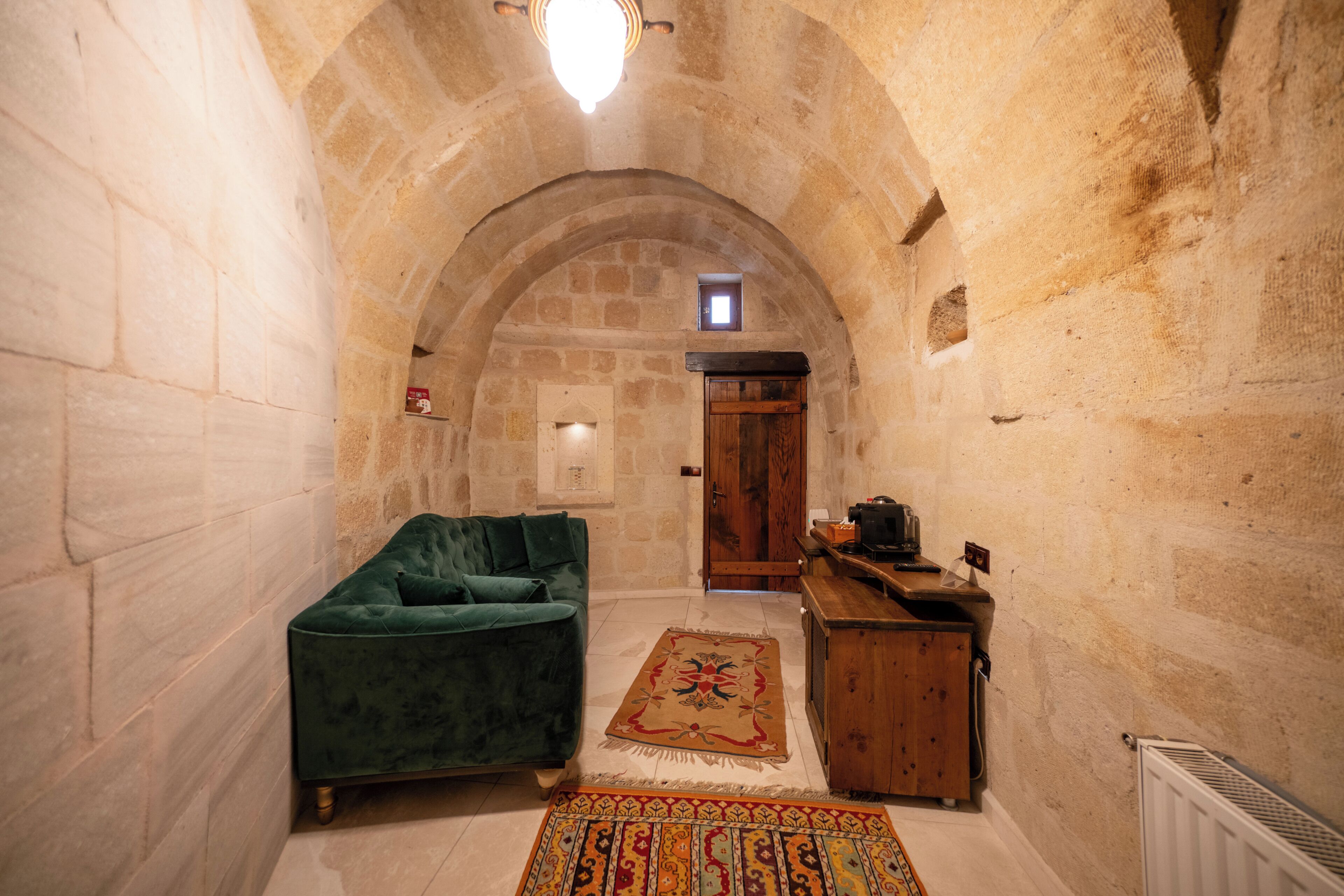 A stone-walled room with a green sofa, a wooden cabinet, and a patterned rug.