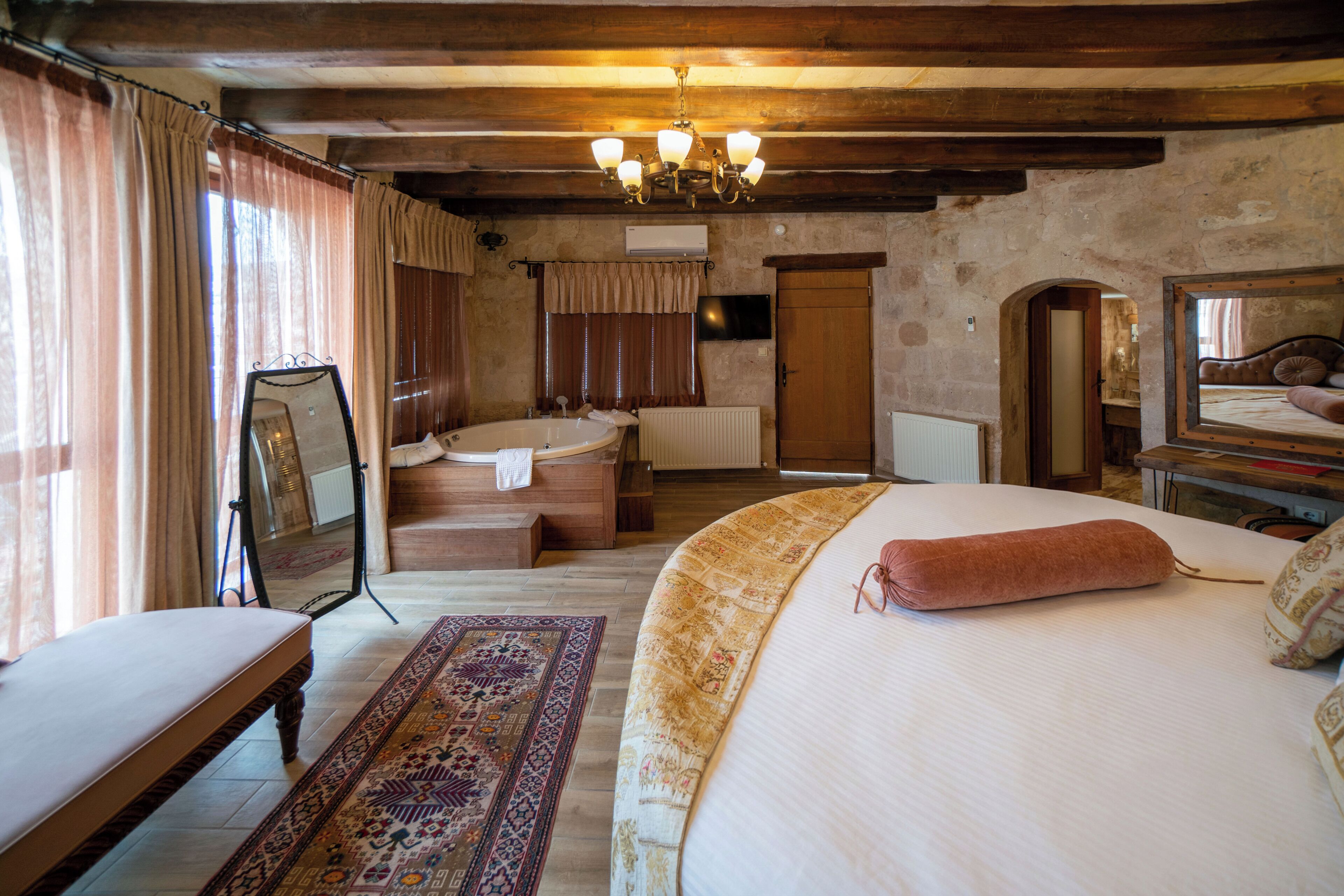 A bedroom with a large bed, a sitting area, a bathtub, and a mirror.