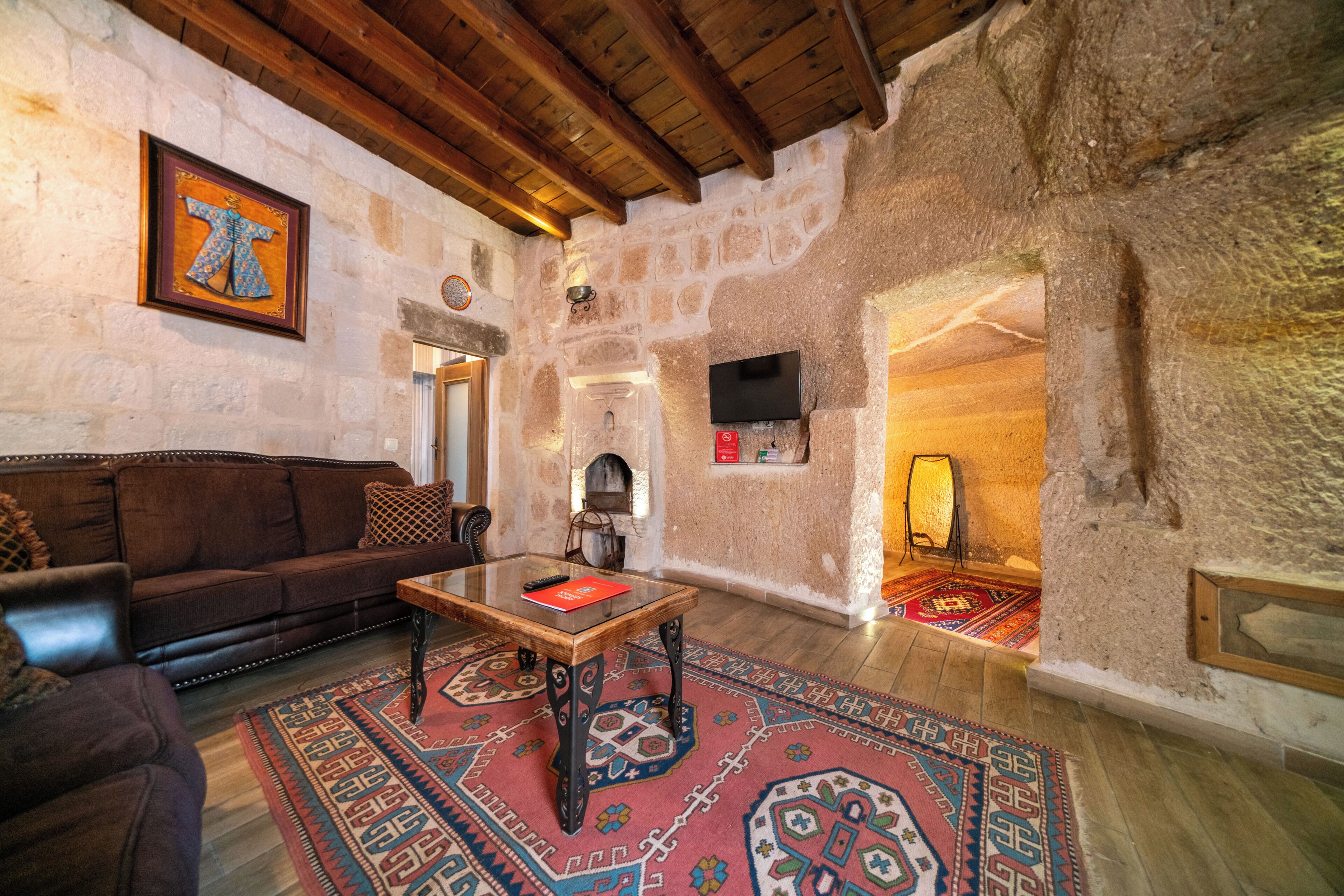 Un intérieur rustique avec des murs en pierre, un plafond en bois, un canapé, une table basse, une cheminée et un téléviseur.