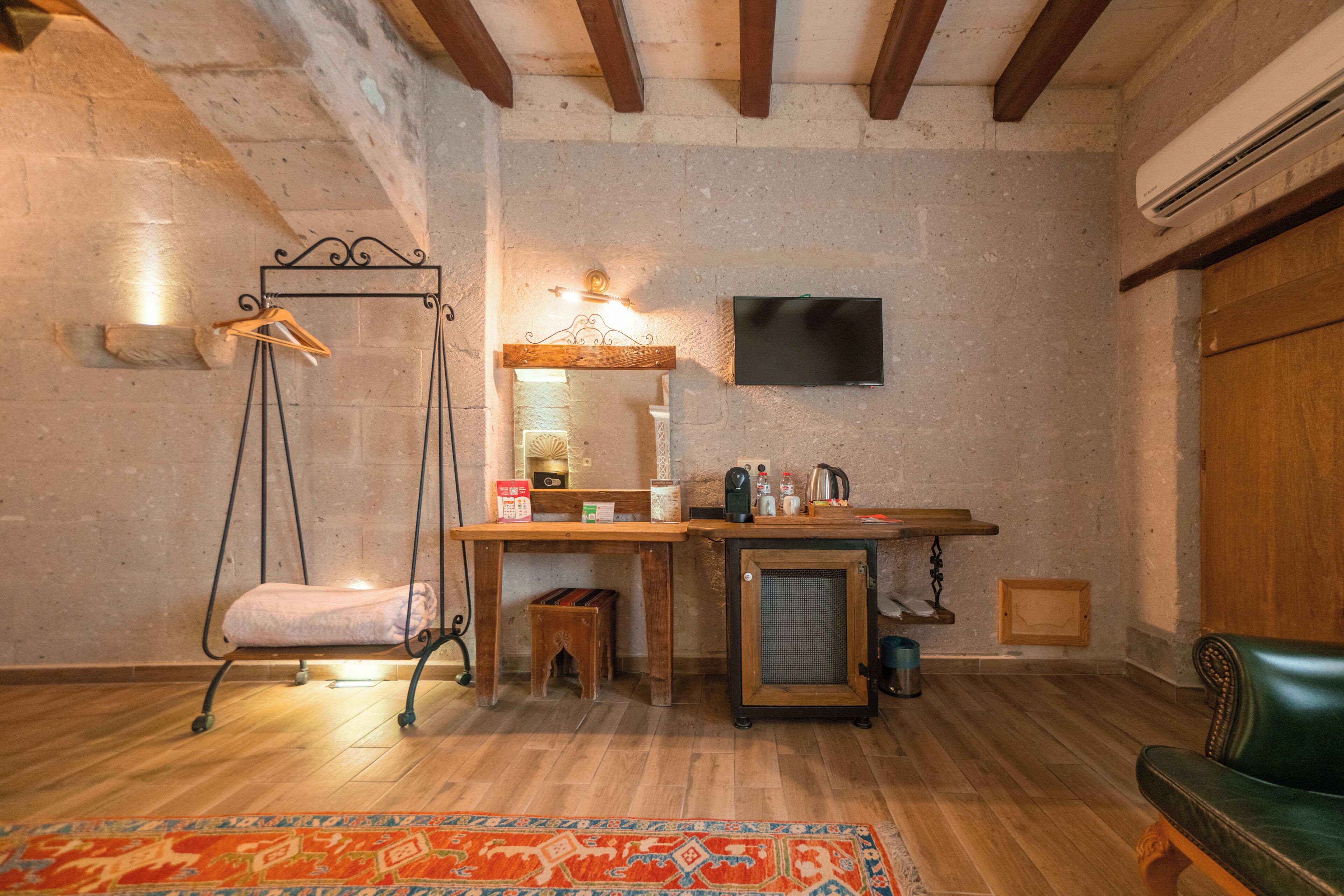 Une pièce comprenant un fauteuil à bascule en bois, un petit tabouret en bois, un bureau en bois avec un miroir, une télévision et un canapé en cuir vert.