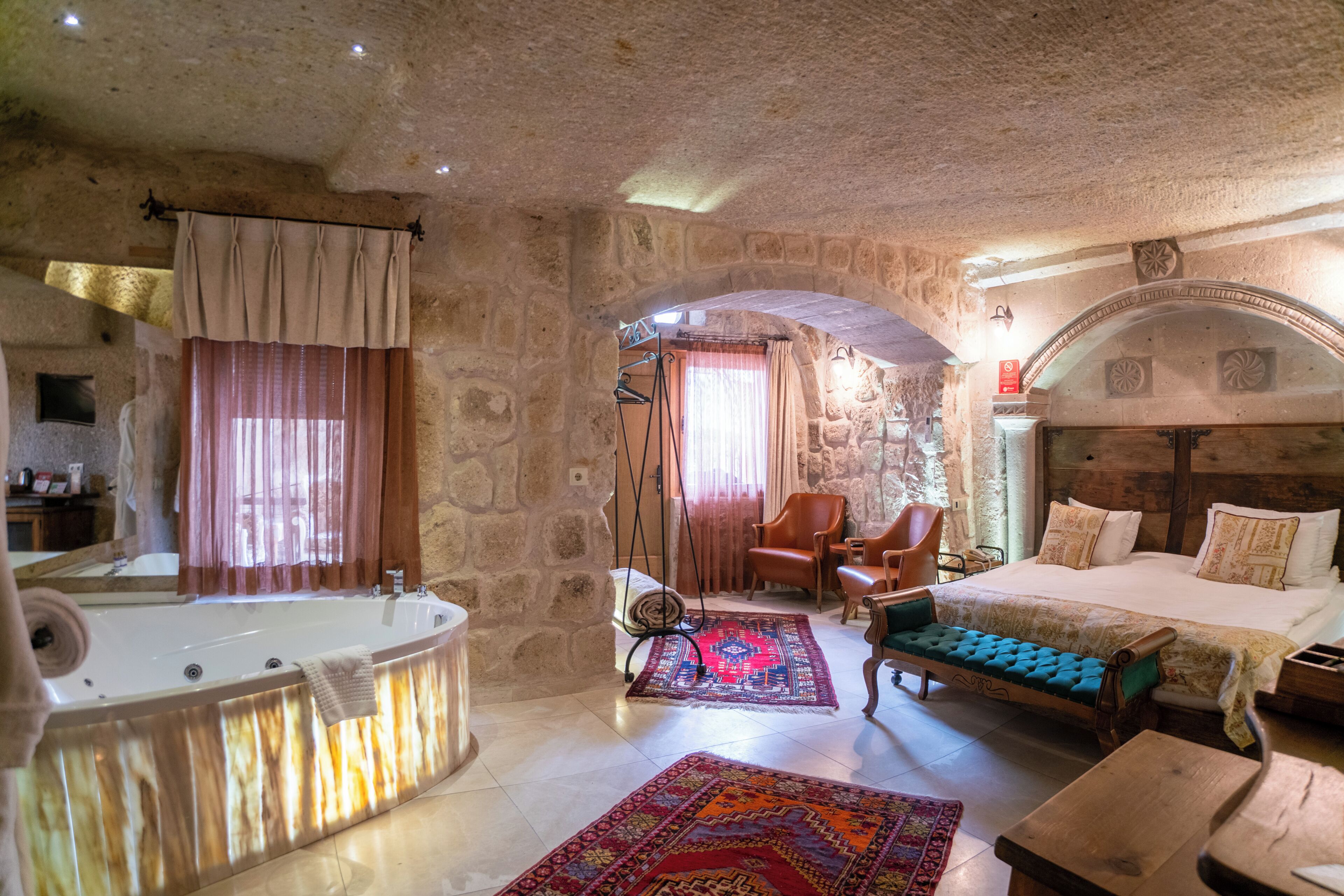 Una habitación con paredes de piedra, una cama, un banco, una silla, una bañera y una pequeña mesa.