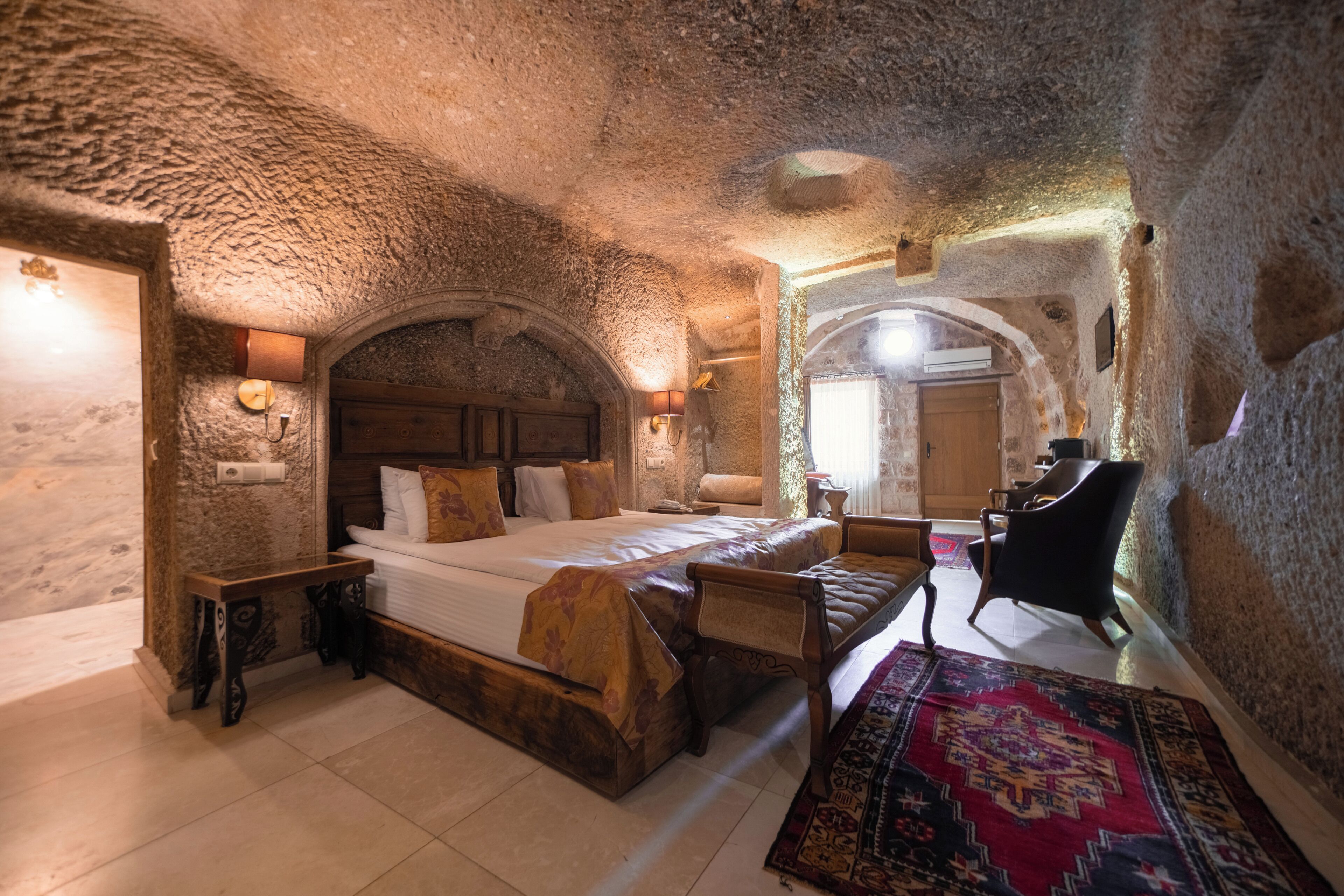 A stone-walled bedroom with a bed, wooden furniture, and a patterned rug.