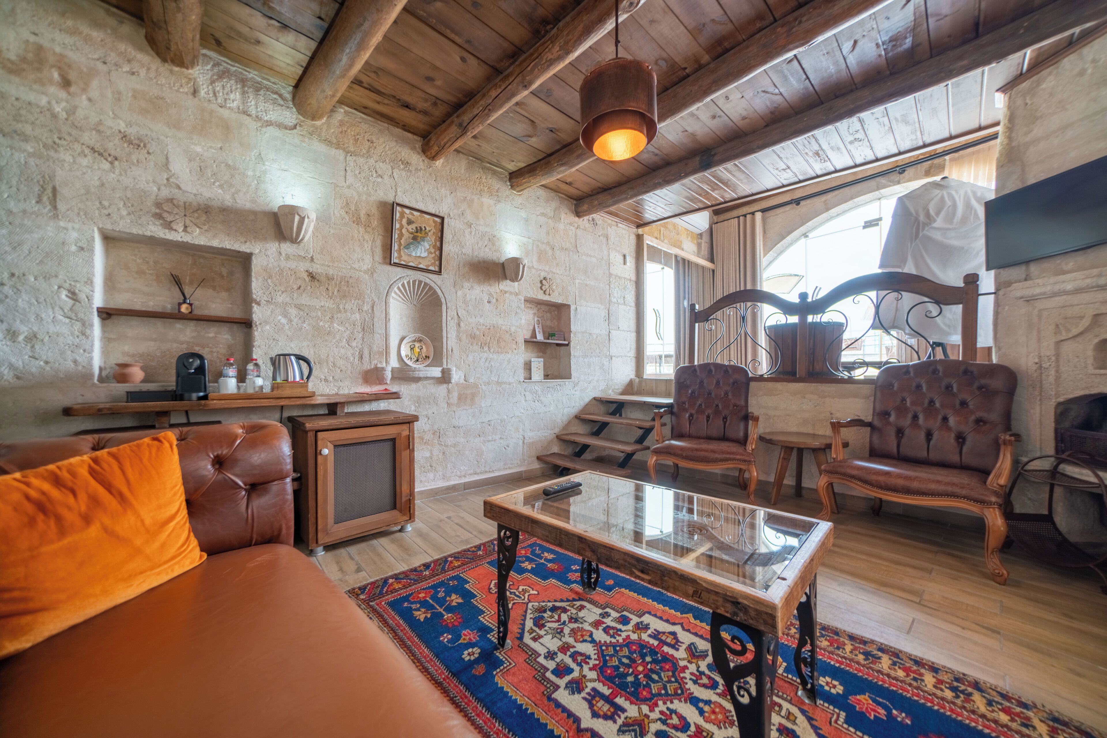 A rustic interior with stone walls, wooden furniture, a glass coffee table, and a fireplace.