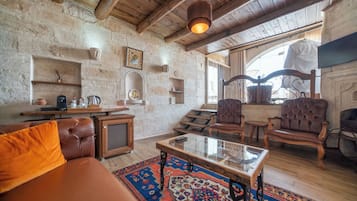 A rustic interior with stone walls, wooden furniture, a glass coffee table, and a fireplace.