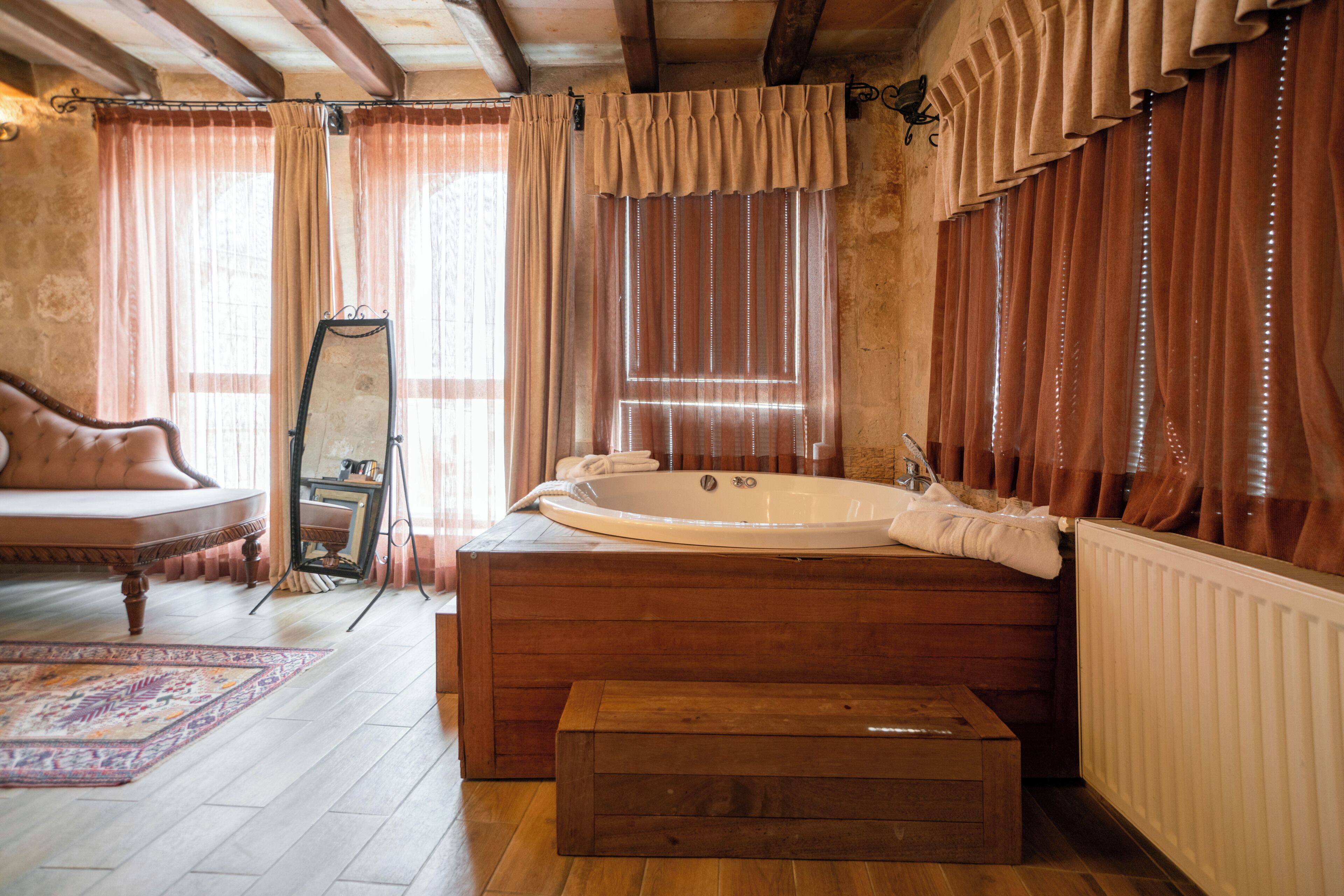 Una habitación con una bañera de madera, un espejo, un sofá y una alfombra estampada.