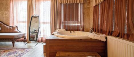 A room with a wooden bathtub, a mirror, a sofa, and a patterned rug.