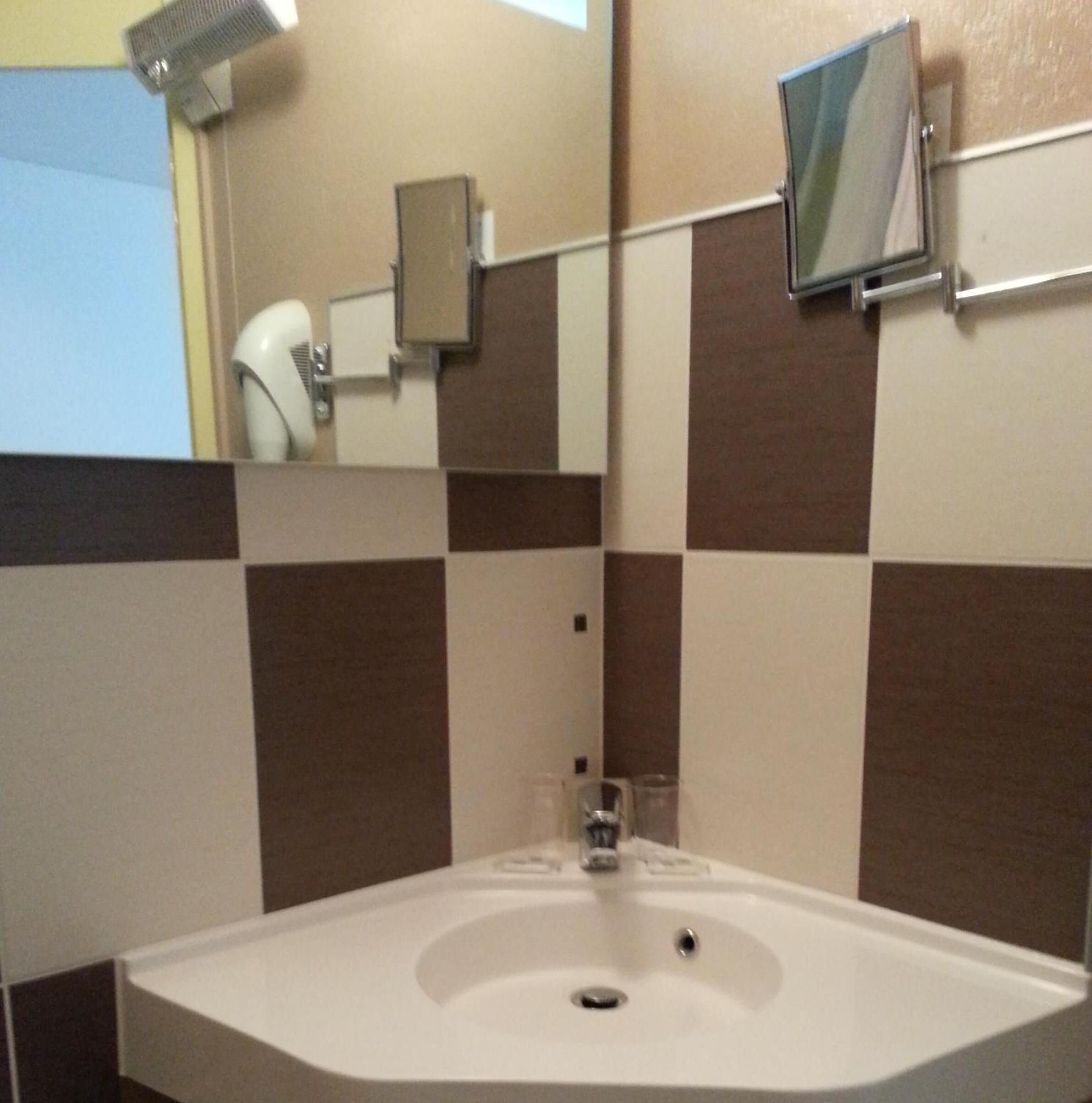 A bathroom with a white sink, a mirror, and a hairdryer mounted on the wall.
