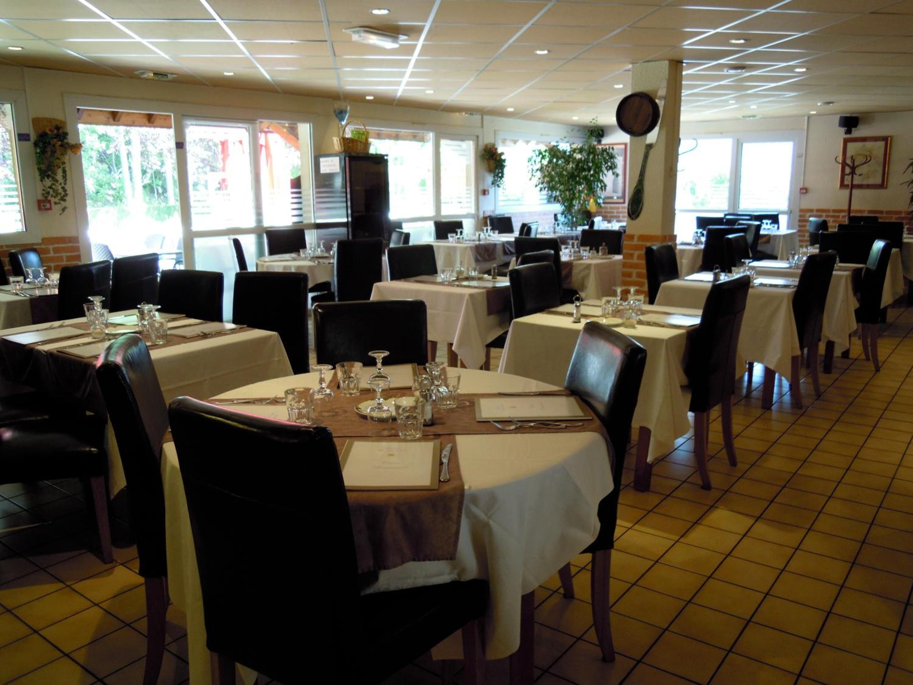 Un ristorante con diversi tavoli apparecchiati, caratterizzato da un pavimento piastrellato e ampie finestre che lasciano entrare luce naturale.