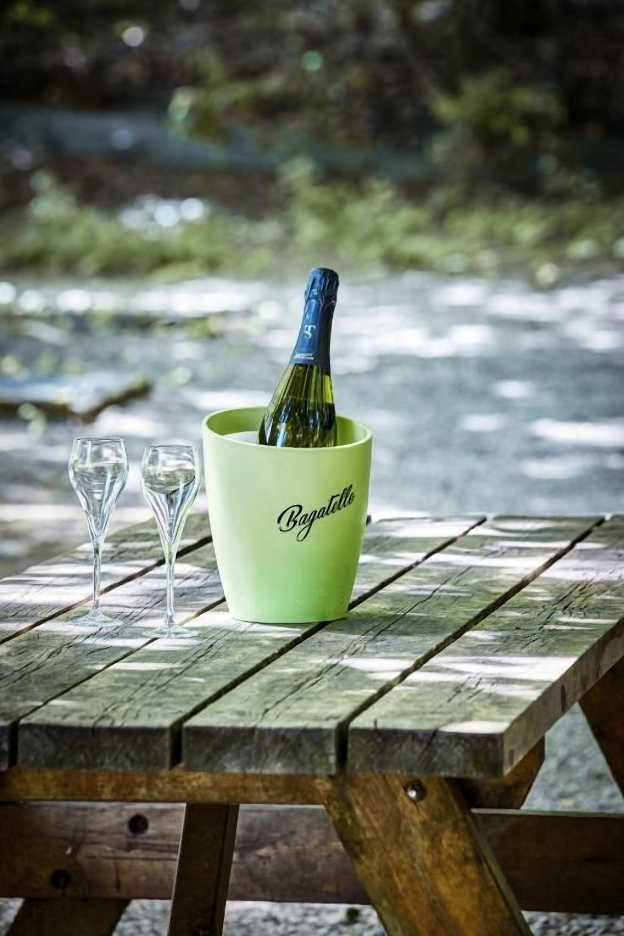 A picnic table with a green container holding a bottle and two glasses.